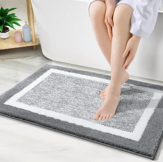 Person sitting on a gray and white textured bath mat in a bathroom setting.